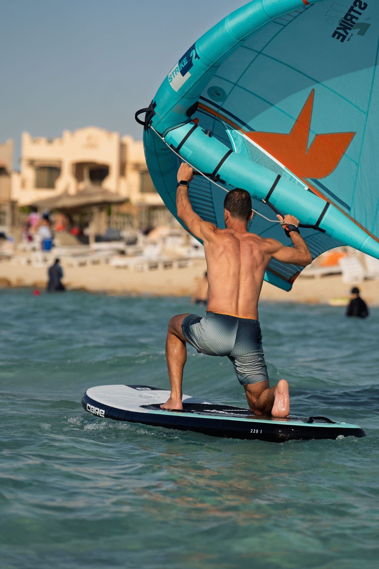 Seen from behind, a rider comes up off their knees on the board with the wing held high.