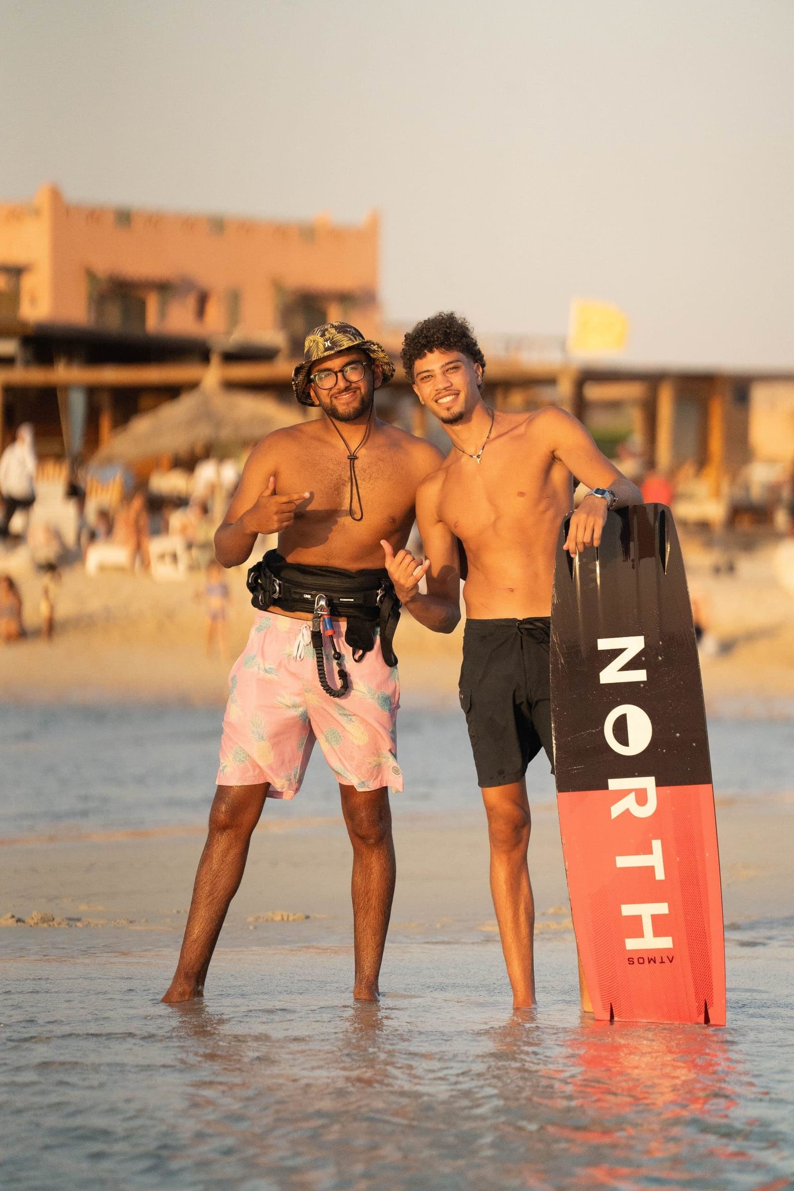Two kitesurfers smile together in shallow water with a board.