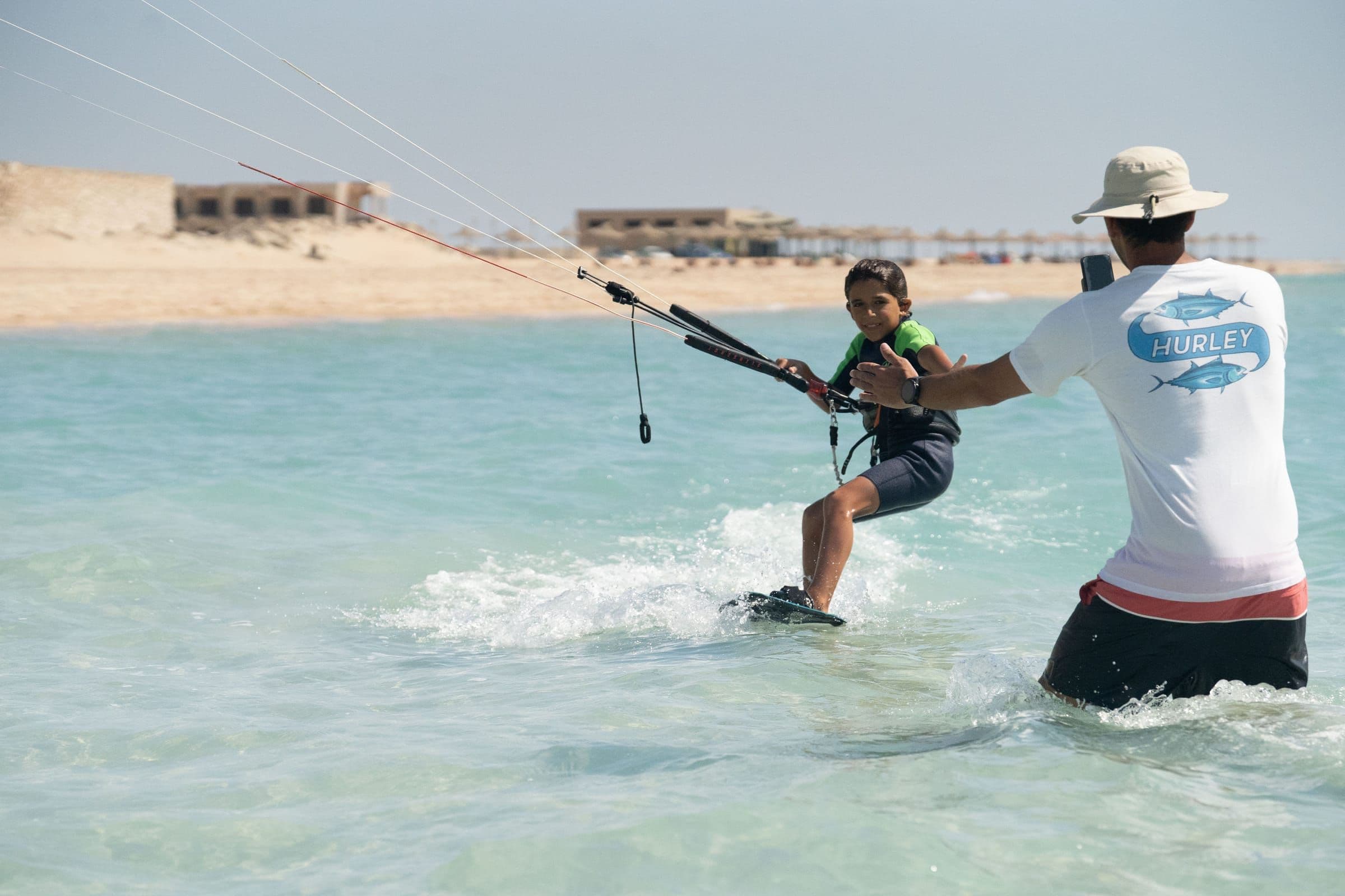 An instructor reaches toward a child learning to ride in shallow water.