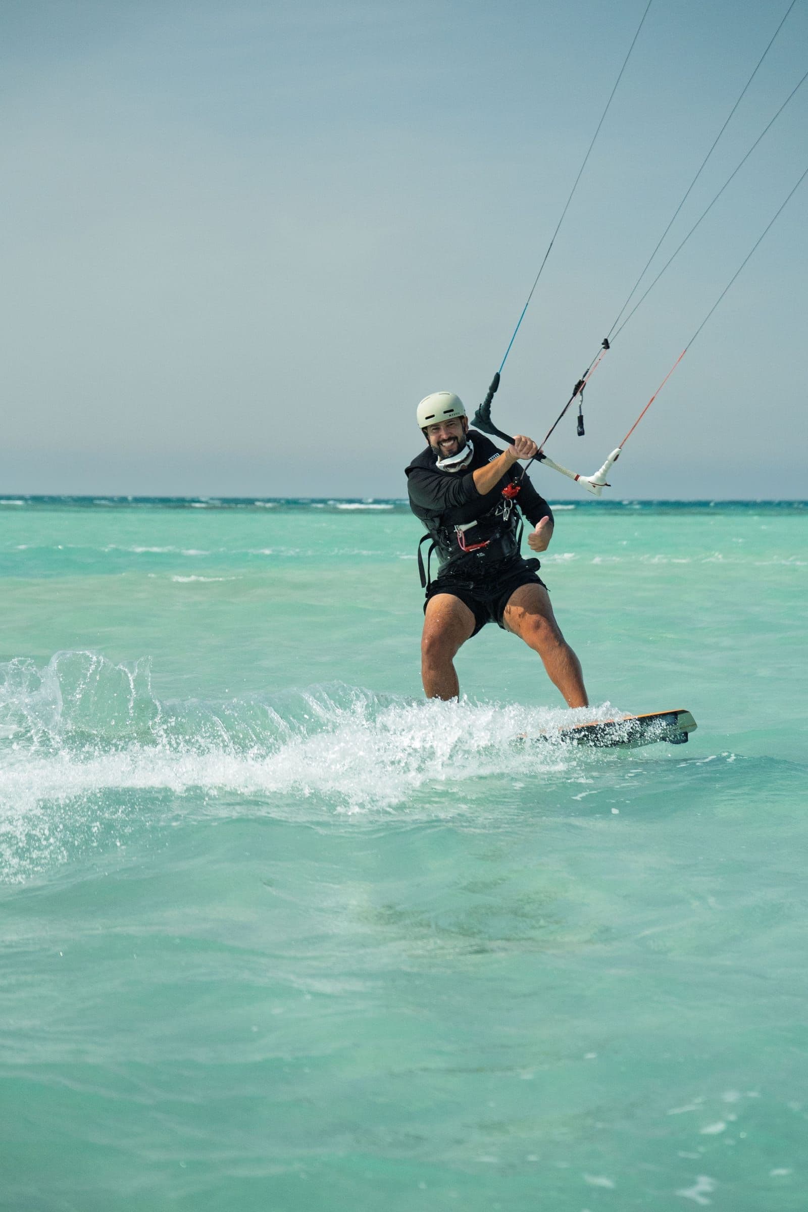 A smiling kitesurfer rides toward the camera across the lagoon.