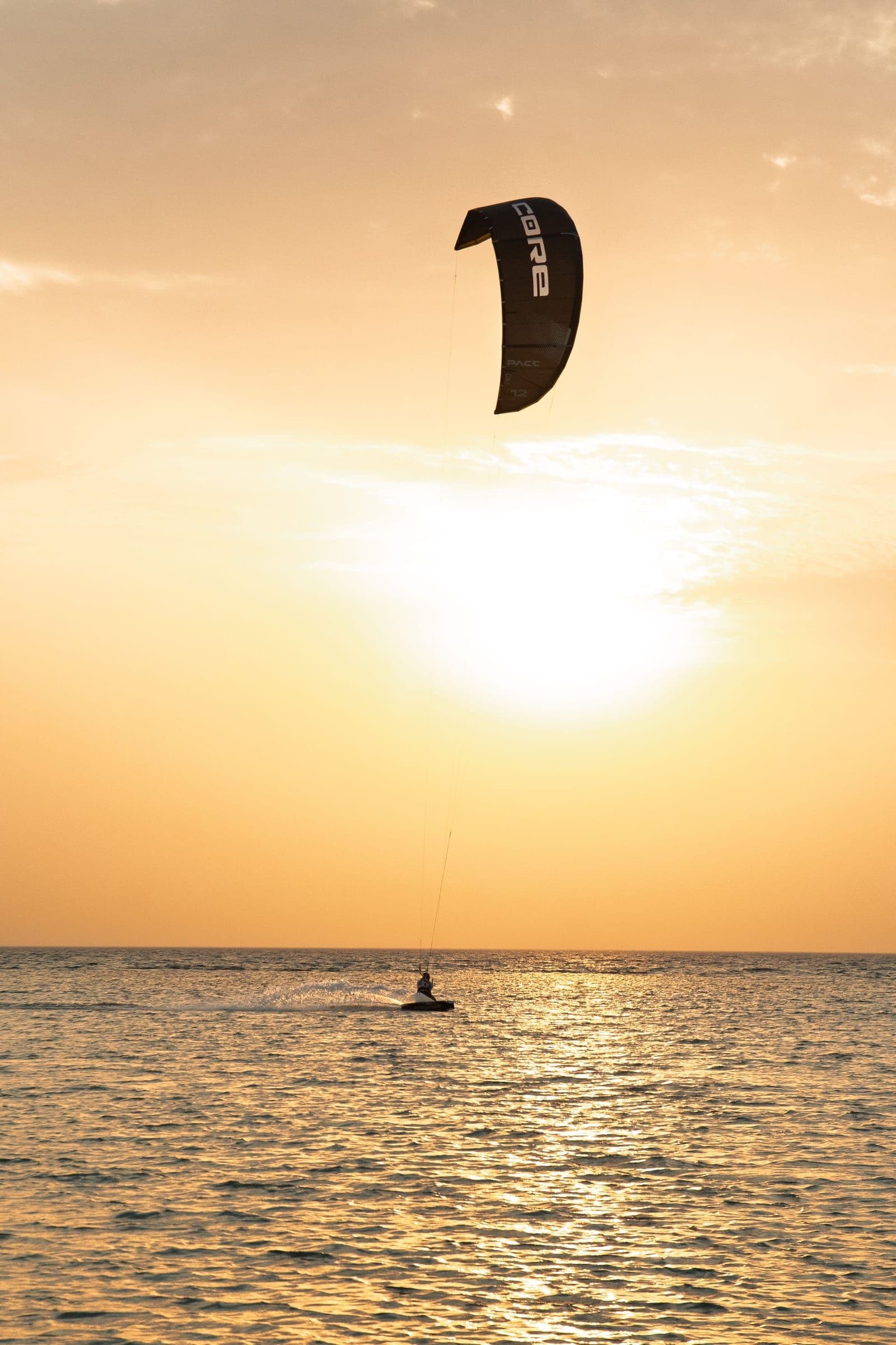 A lone kitesurfer rides beneath a black kite at sunset.